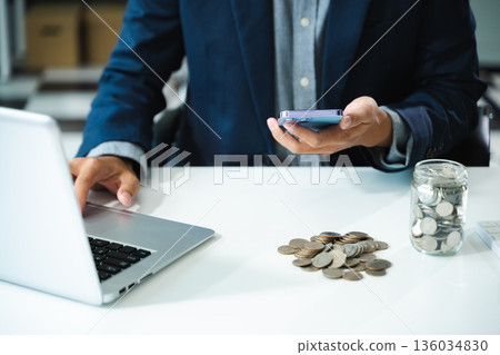 businessman holding coins putting in glass with using smartphone and calculator to calculate concept saving money 136034830