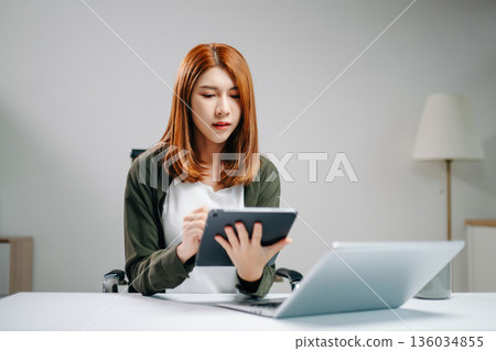 Confident Asian businesswoman working with digital tablet and laptop in bright office. Confident Asian businesswoman working with digital tablet and laptop in bright office. 136034855