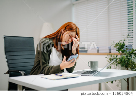 Young Asian woman in office showing signs of stress and burnout while working on laptop. Concept of overwork Young Asian woman in office showing signs of stress and burnout while working on laptop. Concept of overwork 136034864