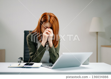 Young Asian woman in office showing signs of stress and burnout while working on laptop. Concept of overwork 136034866