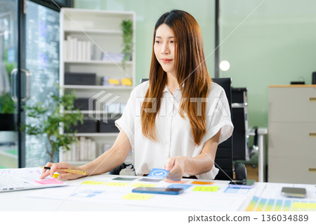 Creative Asian UX UI designer planning mobile app layout with sticky notes, color swatches, and wireframes. Creative Asian UX UI designer planning mobile app layout with sticky notes, color swatches, and wireframes. 136034889