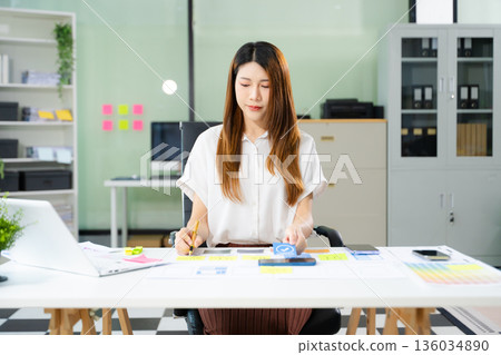 Creative Asian UX UI designer planning mobile app layout with sticky notes, color swatches, and wireframes. Creative Asian UX UI designer planning mobile app layout with sticky notes, color swatches, and wireframes. 136034890