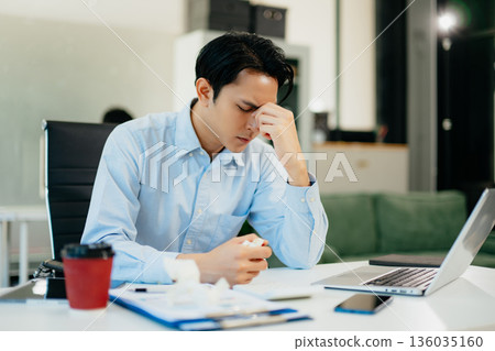 Asian man feeling migraine head strain.Overworked businessman financier while working on laptop and tablet at office. Asian man feeling migraine head strain.Overworked businessman financier while working on laptop and tablet at office. 136035160