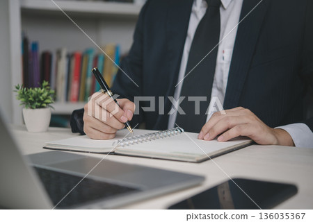 Business executive writing notes in diary at workplace, corporate planning, financial management, office productivity, business success strategy and professional organization. Business executive writing notes in diary at workplace, corporate planning, financial management, office productivity, business success strategy and professional organization. 136035367