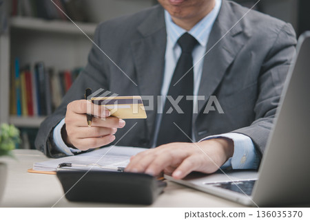 Businessman holding credit card and using calculator in office, online payment, financial transaction, e-commerce, banking service, digital finance, corporate money management concept. 136035370