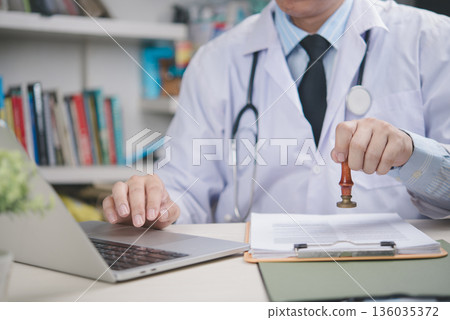 Doctor stamping medical document in office, confirming approval, healthcare certification, hospital paperwork validation, professional authority, legal record and patient management concept. Doctor stamping medical document in office, confirming approval, healthcare certification, hospital paperwork validation, professional authority, legal record and patient management concept. 136035372