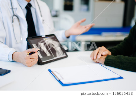 Doctor showing and explaining bone X-ray results to patient during medical consultation. Ideal for healthcare, orthopedic Doctor showing and explaining bone X-ray results to patient during medical consultation. Ideal for healthcare, orthopedic 136035438
