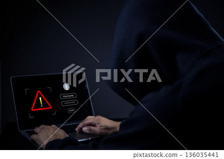 Cybersecurity threat, unknown person in dark hoodie typing on computer, digital safety, cybercrime, personal data protection, scam alert, hacking attempt, online security risk. 136035441