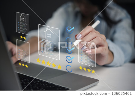woman using a stylus to mark checkboxes and stars while evaluating real estate listings on her laptop. Virtual tools and digital ratings are used to assess the property. 136035461