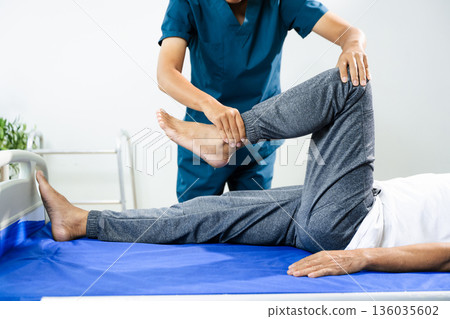 Physiotherapist assists patient with leg and ankle movement therapy during recovery session. Medical care, mobility training, and muscle rehabilitation 136035602