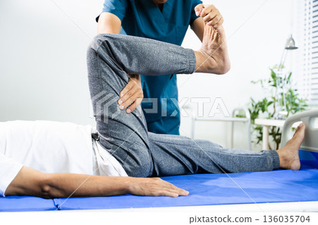 Physiotherapist assists patient with leg and ankle movement therapy during recovery session. Medical care, mobility training, and muscle rehabilitation Physiotherapist assists patient with leg and ankle movement therapy during recovery session. Medical care, mobility training, and muscle rehabilitation 136035704