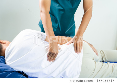 Male physiotherapist applies manual therapy on patient's back during rehab session. Spine care, posture alignment, and muscle relief 136035717