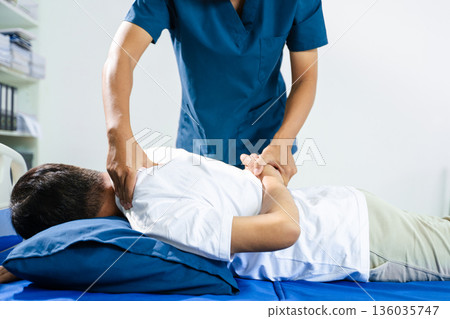 Male physiotherapist performs spine and arm adjustment therapy for patient on bed. Manual therapy, pain relief, posture alignment 136035747