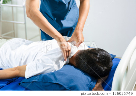 Male physiotherapist performs spine and arm adjustment therapy for patient on bed. Manual therapy, pain relief, posture alignment 136035749