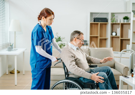 A professional nurse in blue uniform consults with a senior wheelchair patient at home, showcasing real people, empathy, and quality medical care 136035817
