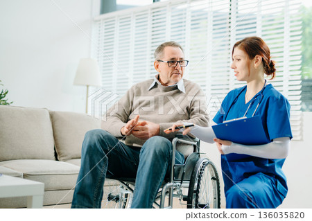 A professional nurse in blue uniform consults with a senior wheelchair patient at home, showcasing real people, empathy, and quality medical care 136035820