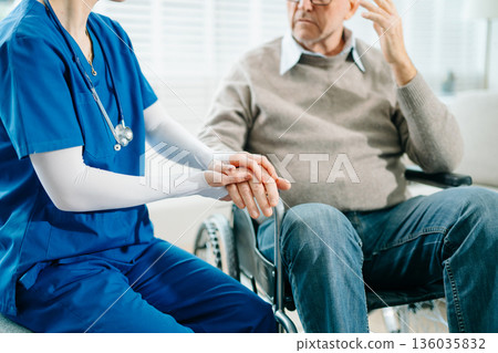A compassionate nurse in blue scrubs holds the hand of a senior patient in a hospital clinic, showcasing real people A compassionate nurse in blue scrubs holds the hand of a senior patient in a hospital clinic, showcasing real people 136035832