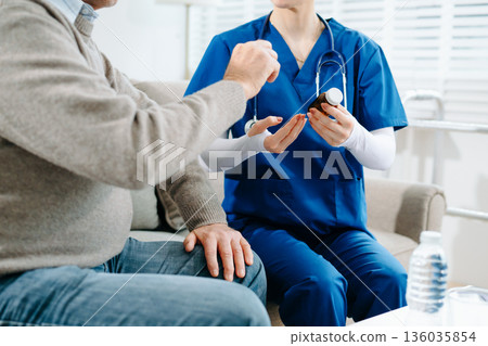 Nurse in blue scrubs reviews medication with an elderly patient at home, showcasing real people, compassionate care 136035854