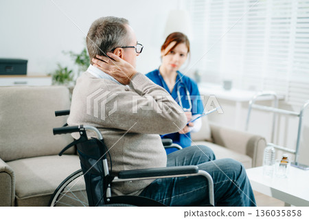 A caring nurse in blue scrubs conducts a neck pain consultation with a senior wheelchair patient at home A caring nurse in blue scrubs conducts a neck pain consultation with a senior wheelchair patient at home 136035858