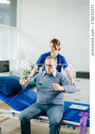 Home physiotherapy: Nurse in blue scrubs guides an elderly patient through resistance band exercises, showcasing real people, mobility Home physiotherapy: Nurse in blue scrubs guides an elderly patient through resistance band exercises, showcasing real people, mobility 136035871