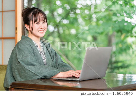 A woman in a yukata working on a computer in a room at a hot spring inn 136035940