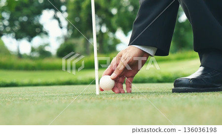 Businessman playing Golf ball practice hit swing on tee in golf club outdoor green field with recreation sport training course. Business men with black Suit driving golf Hobbies 136036198