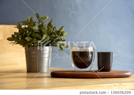 Hot black coffee cup on Wood office desk plant pot decor table blue background. Cup of Black Tea Green potted plant on office wooden desk springtime garden. freshness Home workplace decorate table 136036209