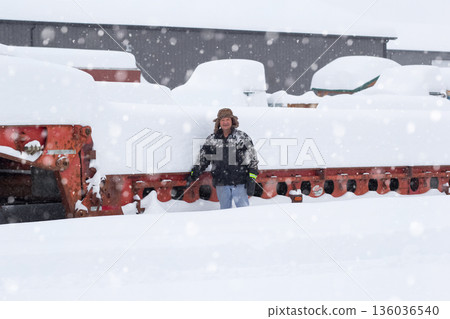 Grain farmer stands in the yard with equipment in heavy snow. Grain farmer stands in the yard with equipment in heavy snow. 136036540