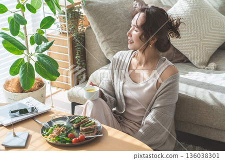 Stylish young Asian woman eating at the living room table 136038301