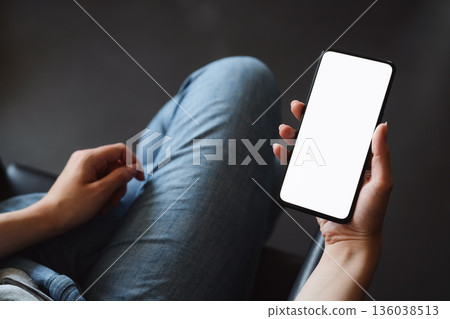 Young woman hold smarphone with white screen while sitting in a chair Young woman hold smarphone with white screen while sitting in a chair 136038513