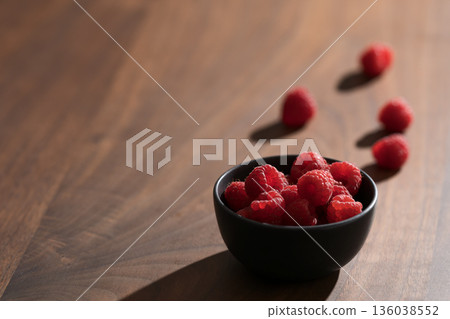Raspberries in black bowl on wooden table closeup 136038552
