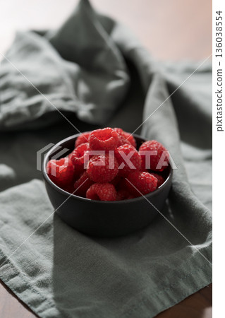 Raspberries in black bowl on linen napkin closeup Raspberries in black bowl on linen napkin closeup 136038554