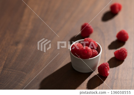 Fresh raspberries in small white bowl on wood table closeup 136038555