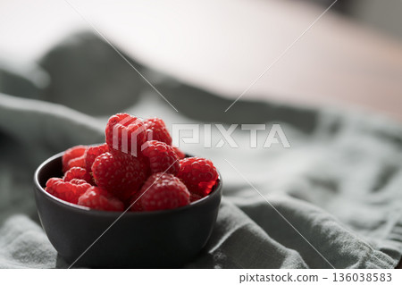 Raspberries in black bowl on linen napkin closeup Raspberries in black bowl on linen napkin closeup 136038583