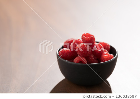 Raspberries in black bowl on wooden table closeup 136038597
