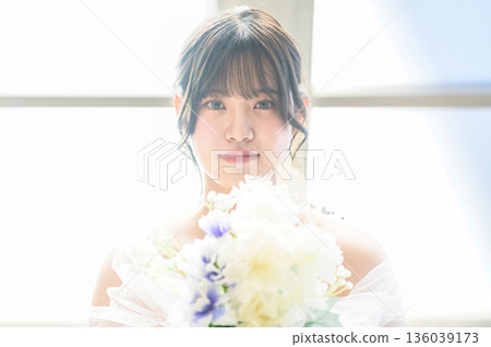 A woman in a wedding dress holding a bouquet by the window A woman in a wedding dress holding a bouquet by the window 136039173