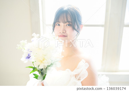 A woman in a wedding dress holding a bouquet by the window A woman in a wedding dress holding a bouquet by the window 136039174