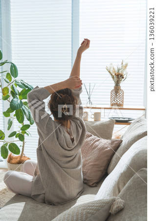 一位女士坐在客廳沙發上伸展身體的背影 136039221