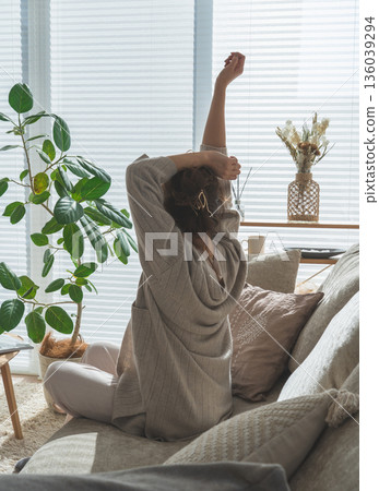 Rear view of a woman stretching while sitting on a sofa in the living room 136039294