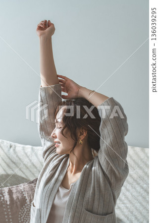 Side profile of a woman stretching while sitting on a sofa in the living room Side profile of a woman stretching while sitting on a sofa in the living room 136039295