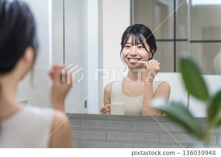 一位年輕的亞洲女性在浴室裡對著鏡子刷牙。 136039948
