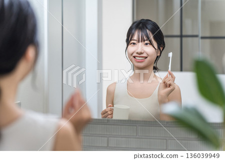 一位年輕的亞洲女性在浴室裡對著鏡子刷牙。 136039949
