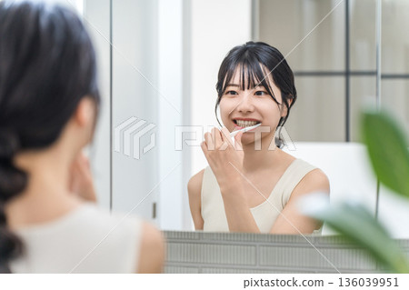 一位年輕的亞洲女性在浴室裡對著鏡子刷牙。 一位年輕的亞洲女性在浴室裡對著鏡子刷牙。 136039951