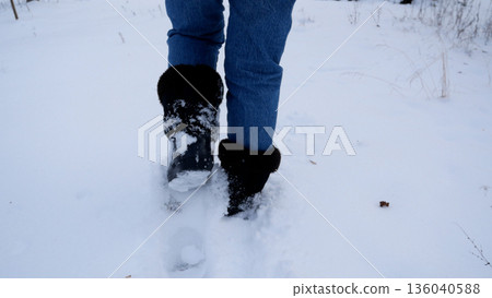 The feet slowly walk in winter warm boots through deep snow. The feet slowly walk in winter warm boots through deep snow. 136040588