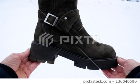 Women's hands holding warm winter boots on thick polyurethane tread  136040590