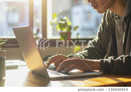 Concentrated typing by a window filled with natural light Concentrated typing by a window filled with natural light 136040954