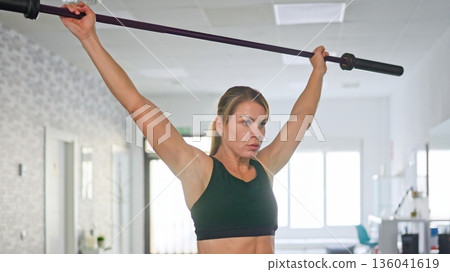 Woman lifting barbell overhead during gym workout session 136041619
