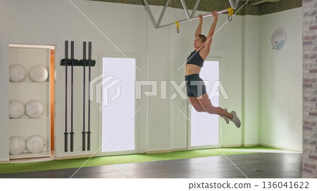 Young woman training kipping exercise in gym Young woman training kipping exercise in gym 136041622