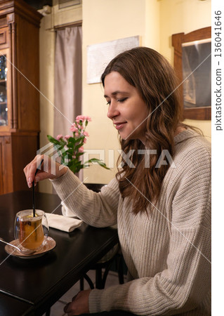 Young woman enjoying hot mulled wine in a cozy cafe interior, warm light, glass mug, winter atmosphere, calm lifestyle moment Young woman enjoying hot mulled wine in a cozy cafe interior, warm light, glass mug, winter atmosphere, calm lifestyle moment 136041646