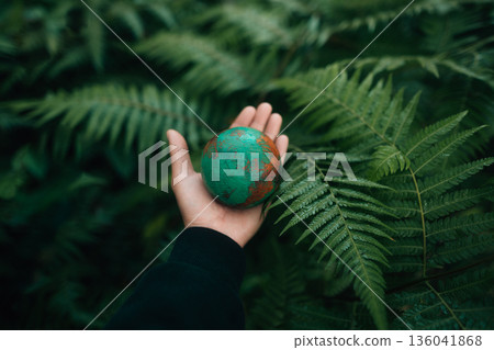 Wooden globe in hand against a fern background, environmental conservation concept. Wooden globe in hand against a fern background, environmental conservation concept. 136041868
